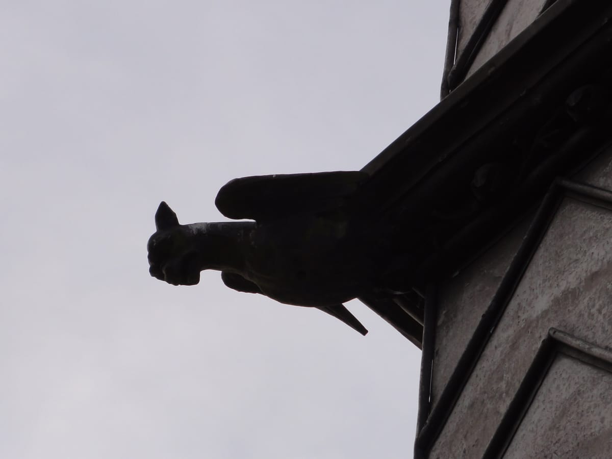 A gargoyle at roof level, in silhouette against a fen sky